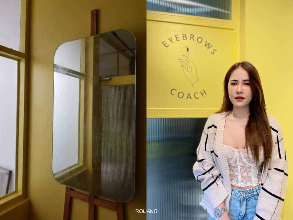 ผู้หญิงคนหนึ่งในสตูดิโอสักคิ้ว 6 มิติกำลังยืนอยู่ข้างกระจกหน้ากำแพงสีเหลือง