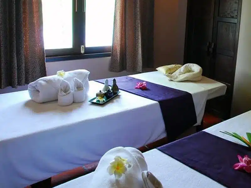 เตียงนวด 2 เตียงในห้องที่มีผ้าขนหนูสีม่วงและดอกไม้ ที่เที่ยวนครปฐม