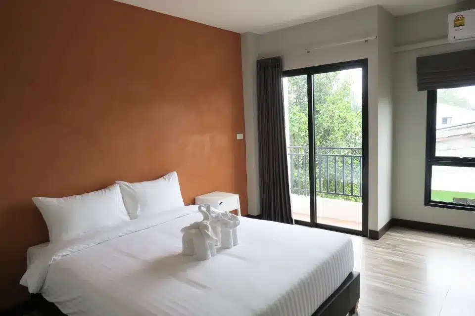 เตียงในห้องที่มีผนังสีส้มและประตูกระจกบานเลื่อน ที่พักตะกั่วป่า