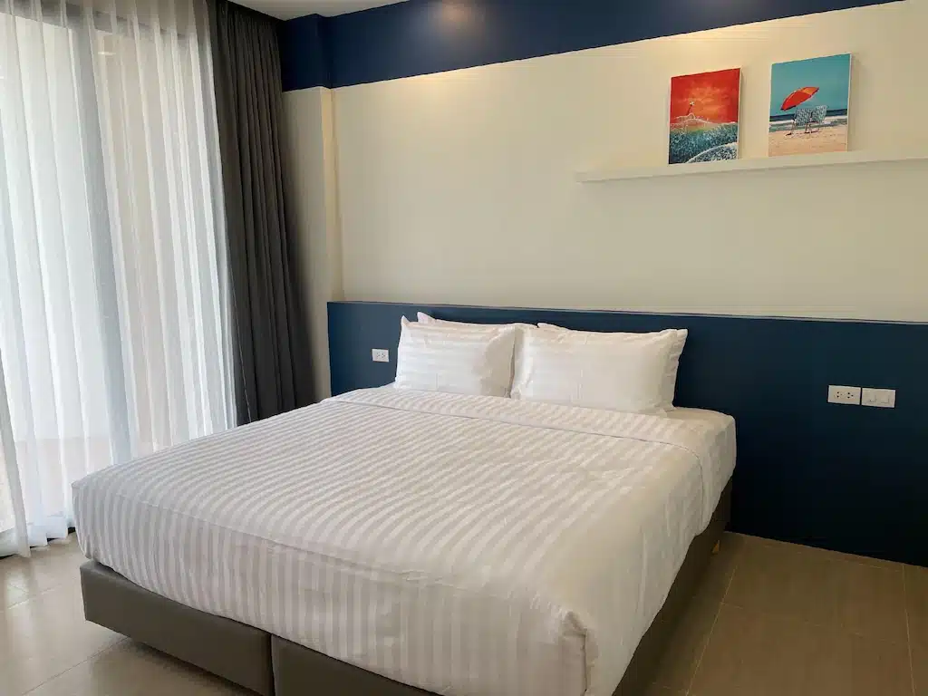ที่พักริมทะเลระยองพร้อมเตียงในห้องที่ประดับด้วยผนังสีน้ำเงินและเครื่องนอนสีขาว ที่พักท่าศาลา