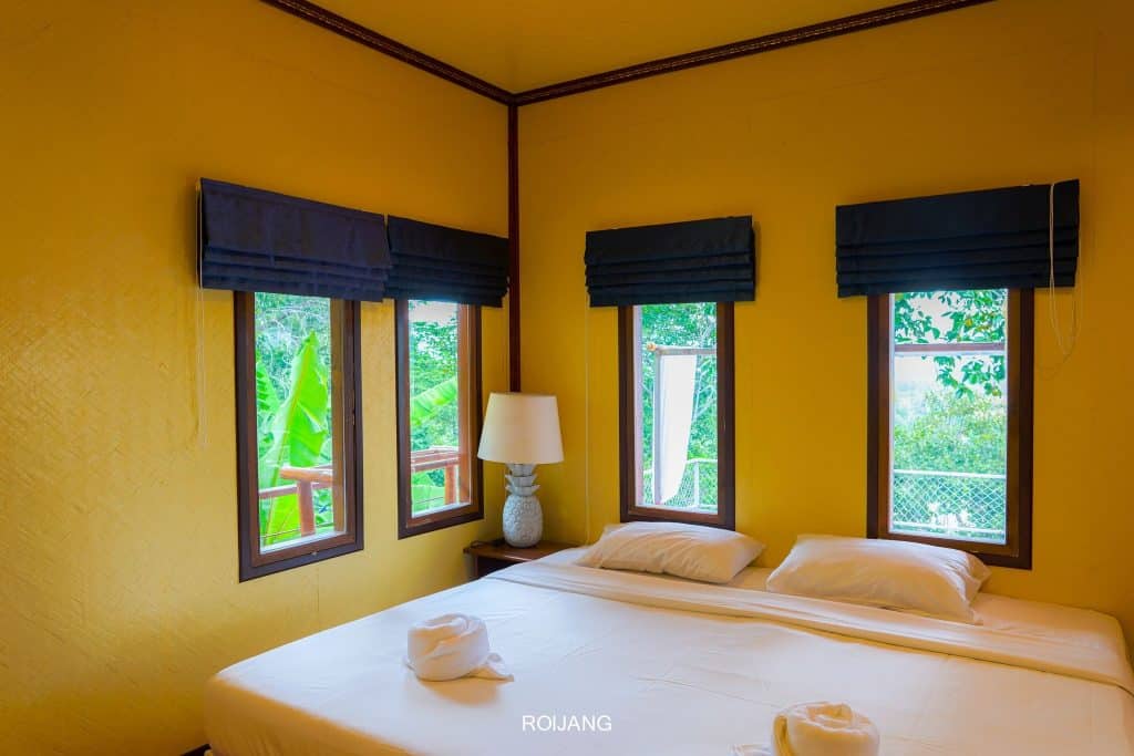 เตียงในห้องที่มีผนังสีเหลืองและหน้าต่างสองบาน โรงแรมตะกั่วป่า