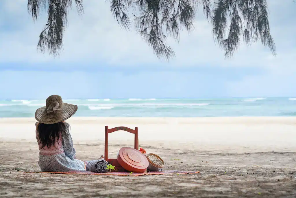 ผู้หญิงนั่งบนชายหาดหรือผู้หญิงนั่งบนชายหาดพร้อมตะกร้า ที่พักภูเก็ตราคาถูก