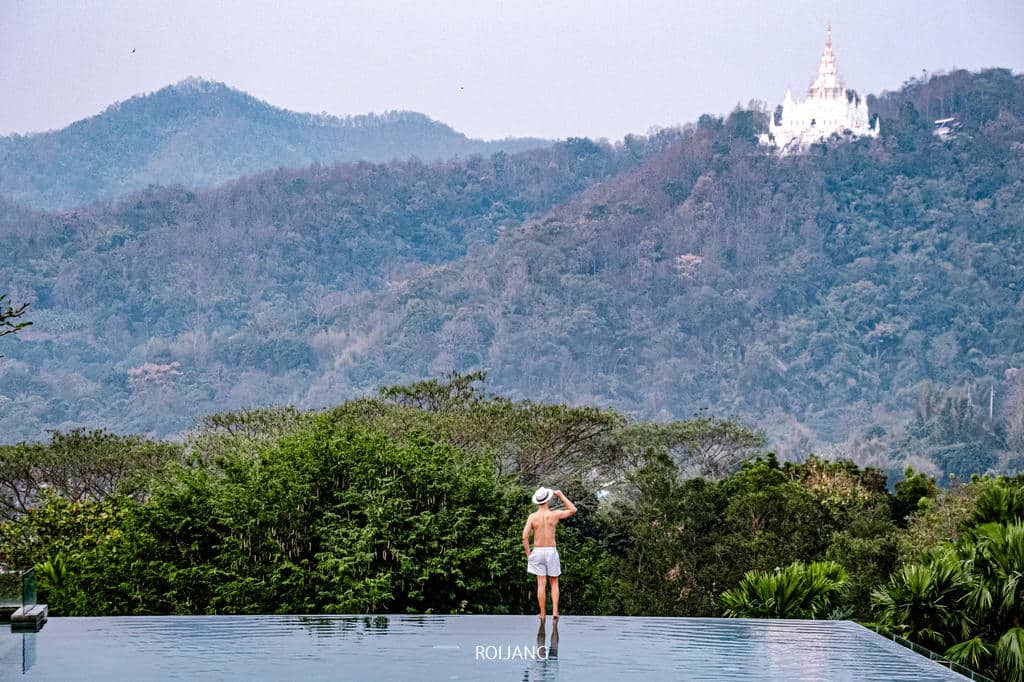ผู้ชายคนหนึ่งยืนอยู่บนขอบสระของวีรันดา ไฮ รีสอร์ท เชียงใหม่ โดยมีภูเขาเป็นฉากหลัง Veranda High Resort Chiangmai