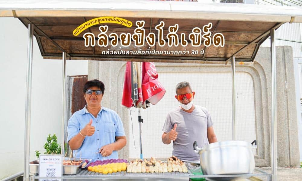ชายสองคนยืนอยู่หน้าแผงขายอาหารที่งาน Phuket Surf Contest 2023 ในประเทศไทย