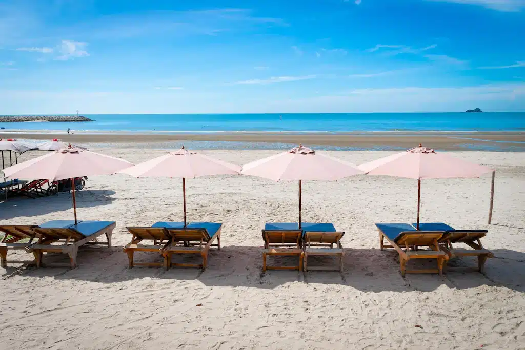 กลุ่มเก้าอี้นั่งเล่นสีสันสดใสบนชายหาดที่สวยงามพร้อมร่มสีชมพู ที่พักหาดสวนสน