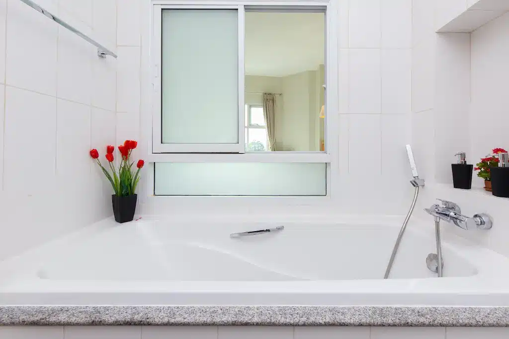 ห้องน้ำสีขาวพร้อมอ่างอาบน้ำและหน้าต่างในเมืองกาญจนบุรี ที่พักเมืองกาญจนบุรี