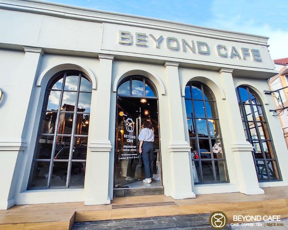 ผู้หญิงยืนอยู่หน้าร้านกาแฟที่เขียนว่า Beyond Cafe ที่เที่ยวอุดร