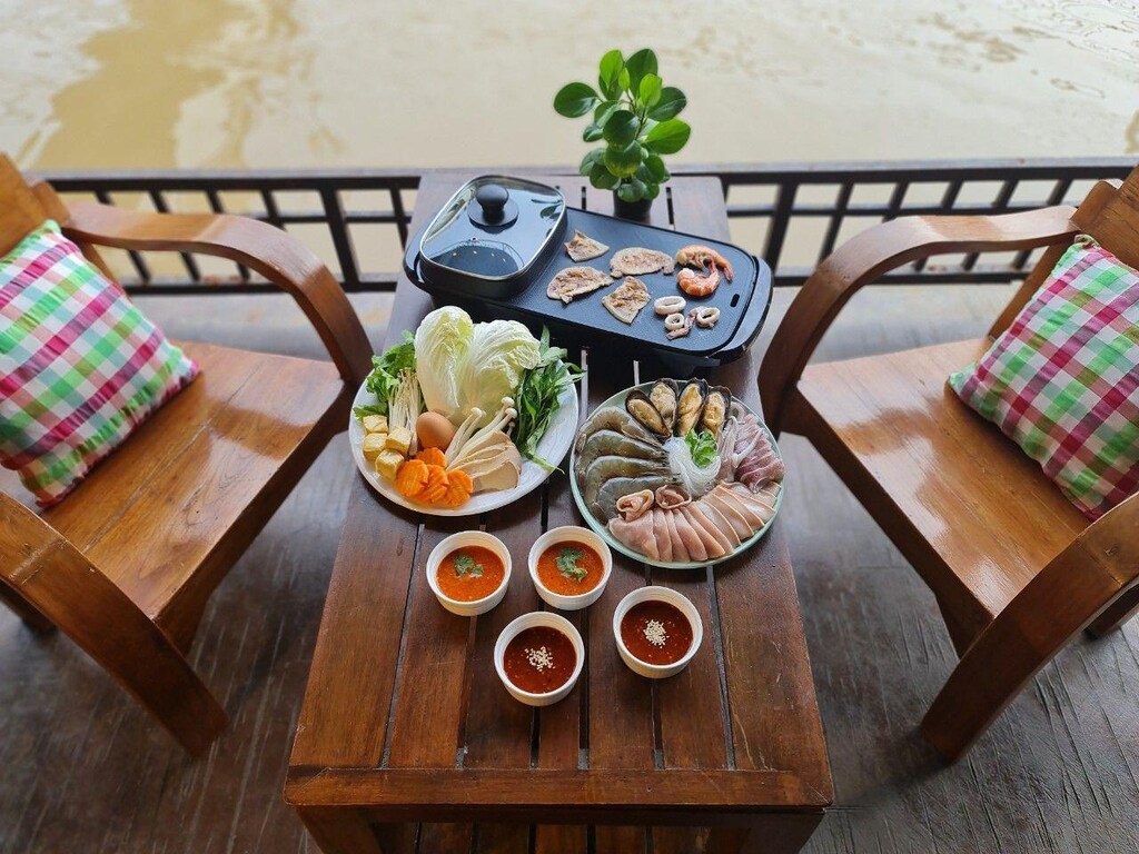 โต๊ะไม้ที่มีอาหารและเครื่องดื่มอยู่ติดกับแม่น้ำ เที่ยวอัมพวา