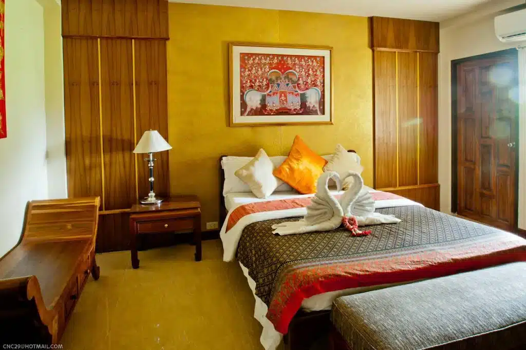 เตียงในห้องที่มีผนังสีเหลืองและหงส์บนเตียง ที่เที่ยวพิจิตร