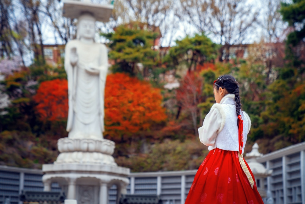 ผู้หญิงในชุดสีแดงยืนอยู่หน้ารูปปั้นในสถานที่ท่องเที่ยวยอดนิยมในเกาหลีใต้ ที่เที่ยวเกาหลี