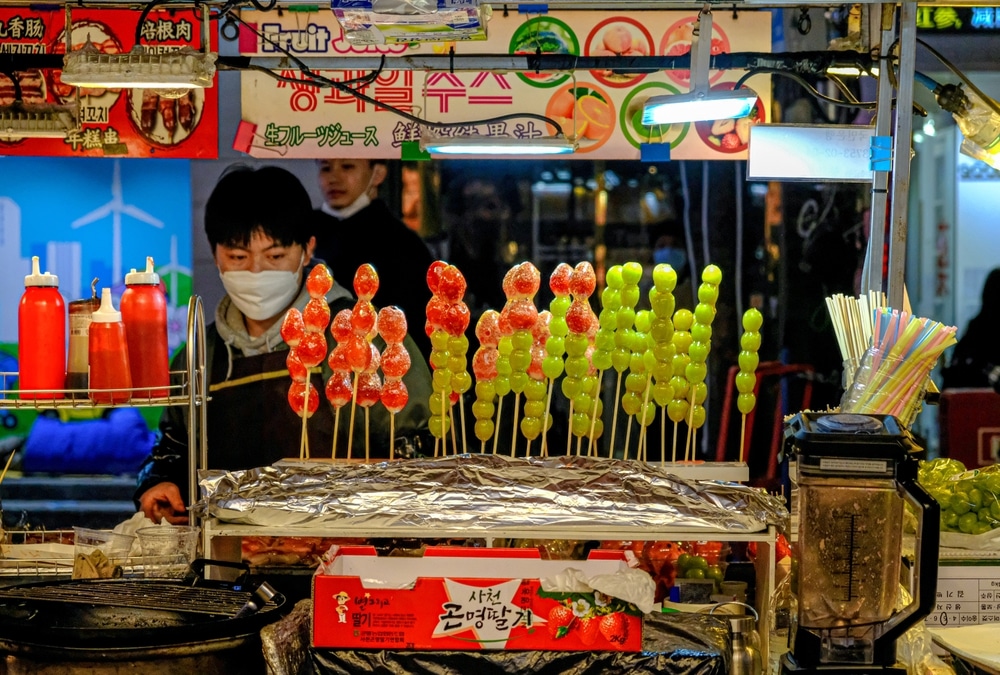 ผู้ชายกำลังยืนอยู่ที่แผงขายอาหารใน เที่ยวเกาหลี (เที่ยวเกาหลี) ที่เที่ยวเกาหลี
