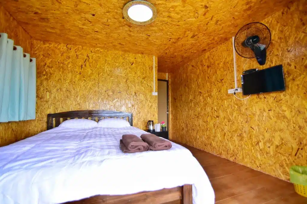 เตียงในห้องที่มีผนังสีเหลืองและพัดลมในชลบุรี ประเทศไทย รีสอร์ทเชียงใหม่บนดอย