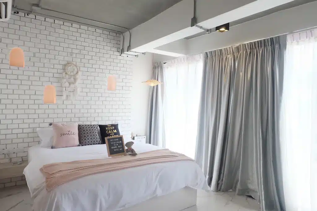 ห้องนอนสีขาวชมพูกับผนังอิฐบนที่พักเกาะลันตา โรงแรมหัวหินติดทะเล