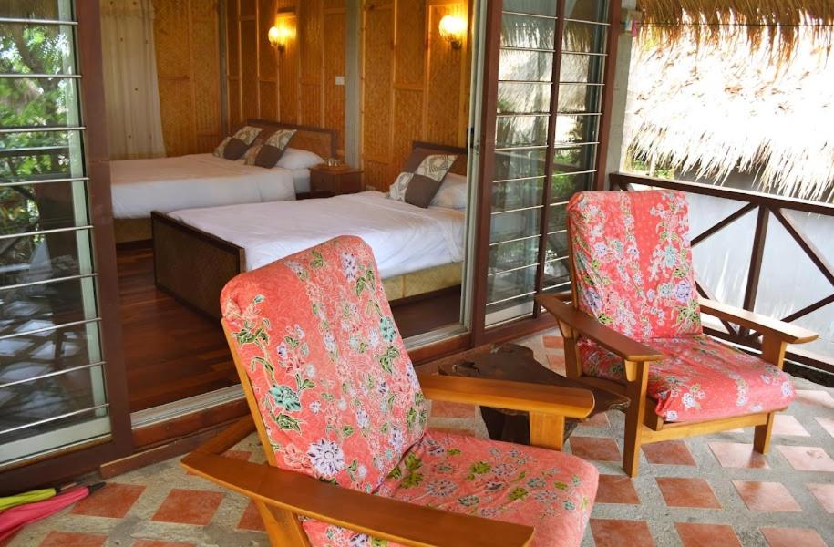 เก้าอี้สองตัวและเตียงในห้องที่มีหลังคามุงจาก ที่พักเกาะลันตาติดทะเล