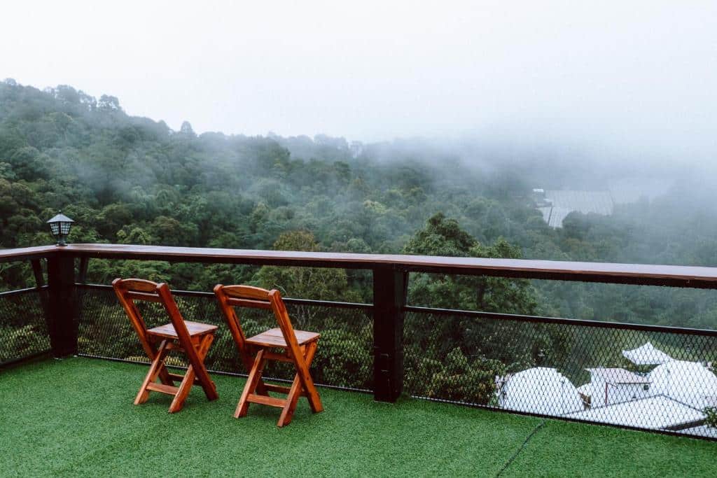 เก้าอี้ไม้สองตัวบนระเบียงที่มองเห็นป่าหมอกในชลบุรีที่เที่ยว ที่พักบนดอยเชียงใหม่ราคาถูก