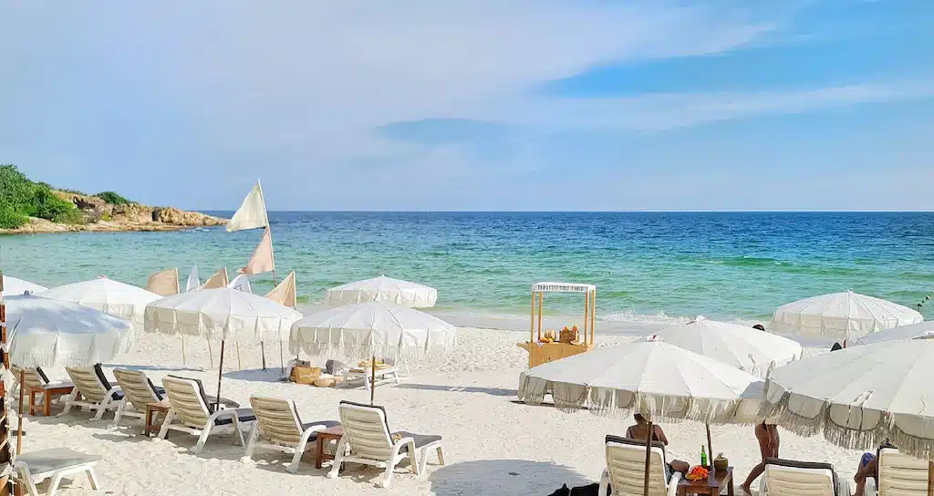 ชายหาดที่มีร่มและเก้าอี้สีขาวบนพื้นทราย ที่พักหาดทรายแก้ว