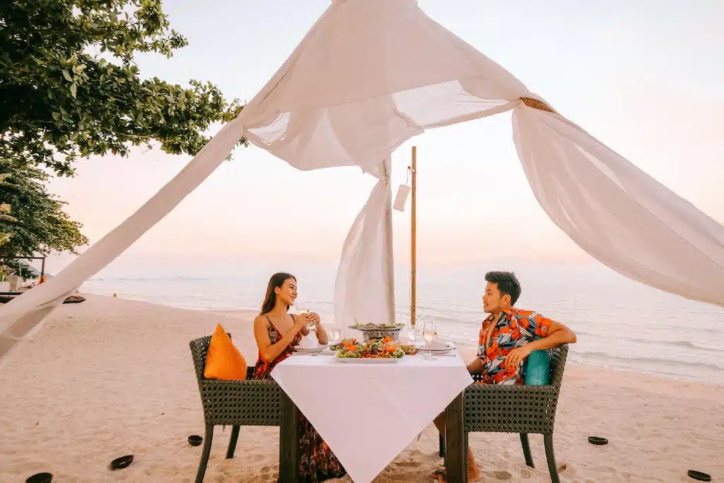 คู่รักนั่งอยู่ที่โต๊ะบนชายหาด ที่พักขนอมติดทะเล