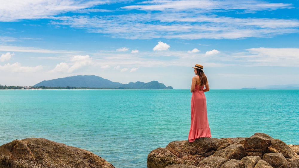 ผู้หญิงในชุดสีชมพูยืนอยู่บนโขดหินที่มองเห็นทะเล ที่พักขนอมติดทะเล