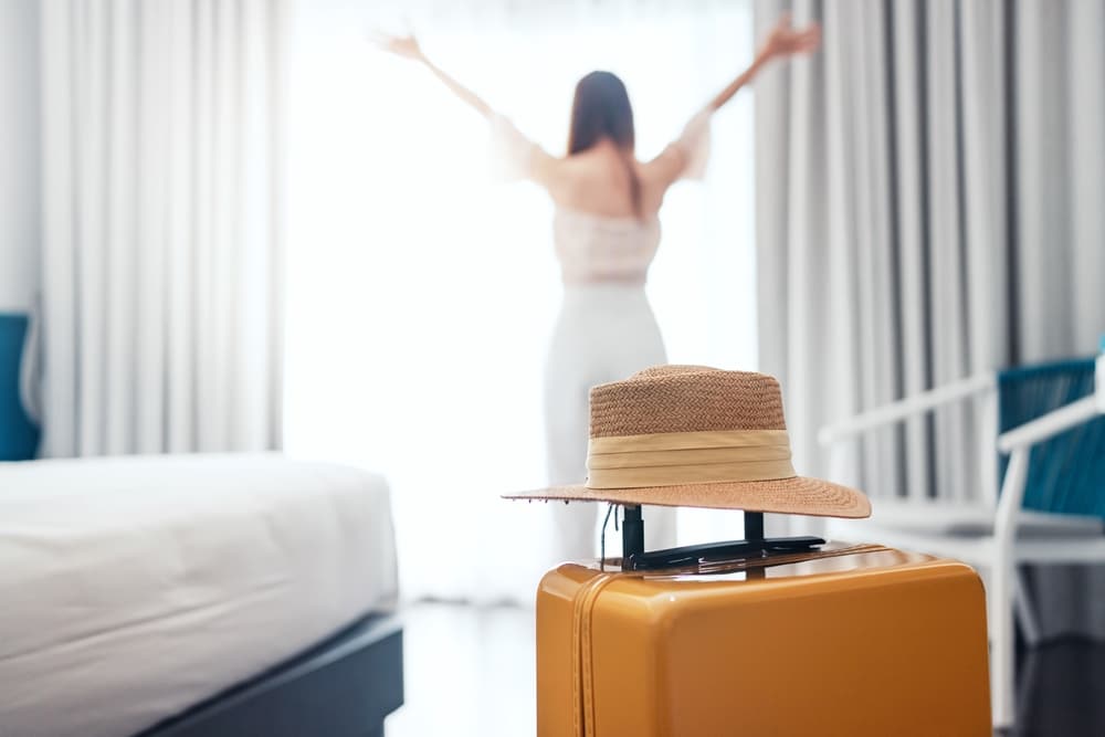ผู้หญิงสวมหมวกยืนอยู่ข้างกระเป๋าเดินทางในห้องพักใน โรงแรมใกล้อิมแพ็คเมืองทองธานี