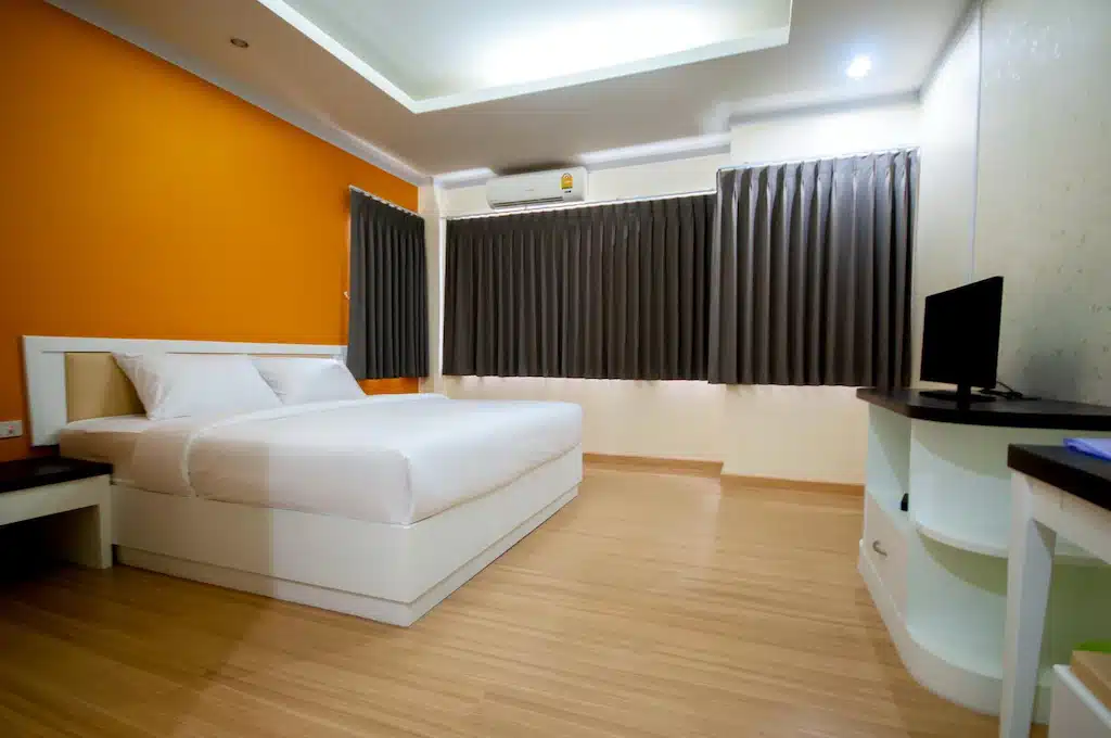 ห้องพักในโรงแรมศรีสะเกษที่มีผนังสีส้มและเตียงสีขาว โรงแรมศรีสะเกษ