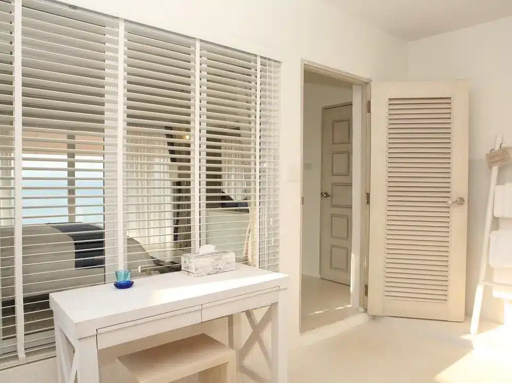 ห้องน้ำสีขาวพร้อมบานประตูหน้าต่างไม้และโต๊ะเครื่องแป้งสีขาวในการควบคุมระนอง ที่พักระนอง