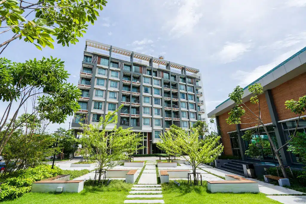อาคารอพาร์ตเมนต์ขนาดใหญ่ที่รายล้อมไปด้วยหญ้าและต้นไม้เขียวขจีในสถานที่ท่องเที่ยวจังหวัดราชบุรี ที่เที่ยวบางแสน