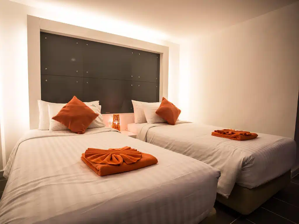 เตียง 2 เตียงพร้อมผ้าเช็ดตัวสีส้มในห้องพักโรงแรมในนครศรีธรรมราช ที่พักนครศรีธรรมราช