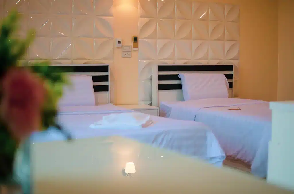 เตียงสองเตียงในห้องที่มีผ้าปูที่นอนสีขาวและดอกไม้อยู่ที่บึงกาฬ ที่พักบึงกาฬ