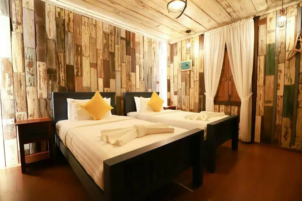 เตียงสองเตียงในห้องเรียบง่ายที่มีผนังไม้ โรงแรมระนอง 