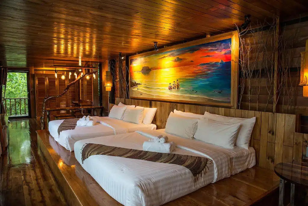 ห้องพักในโรงแรมแสนสบายในจังหวัดตรัง มีเตียงนุ่มสบาย 2 เตียงและภาพวาดอันน่าหลงใหลประดับอยู่บนผนัง ที่พักตรัง