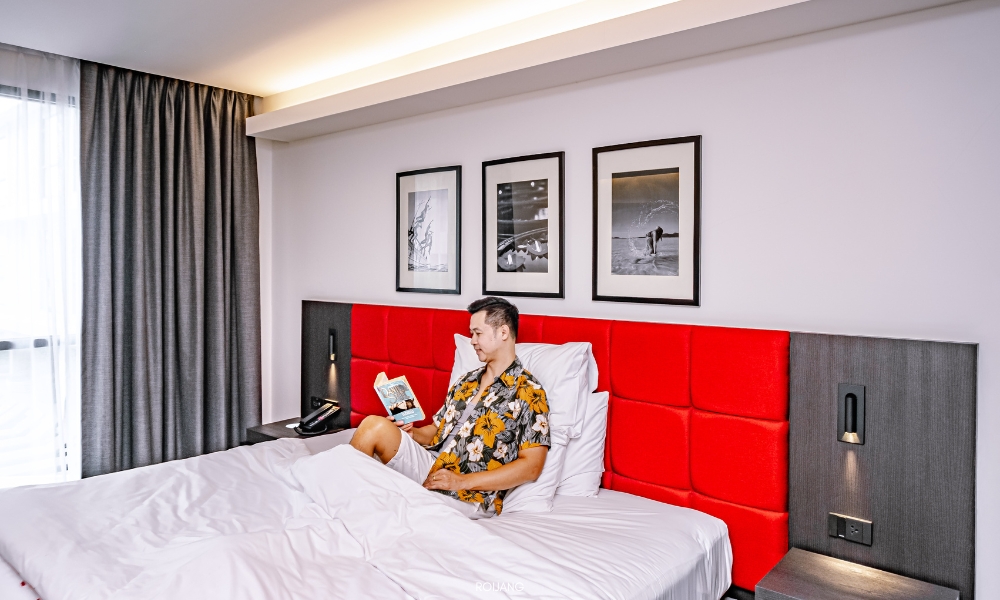 ผู้ชายกำลังอ่านหนังสือบนเตียงในห้องพักในโรงแรม Travelodge Travelodge Phuket Town