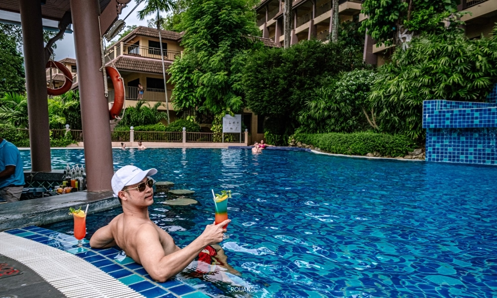 ผู้ชายกำลังนั่งอยู่ในสระว่ายน้ำที่ชนาลัย การ์เดน รีสอร์ท พร้อมเครื่องดื่มอยู่ในมือ Chanalai garden resort