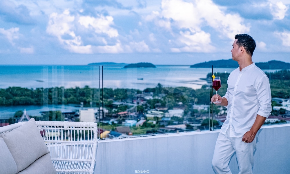 ผู้ชายถือแก้วไวน์บนระเบียงที่มองเห็นวิวทะเลที่โรงแรมโนโวเทล โภคีธรา ภูเก็ต Novotel phokeethra Phuket
