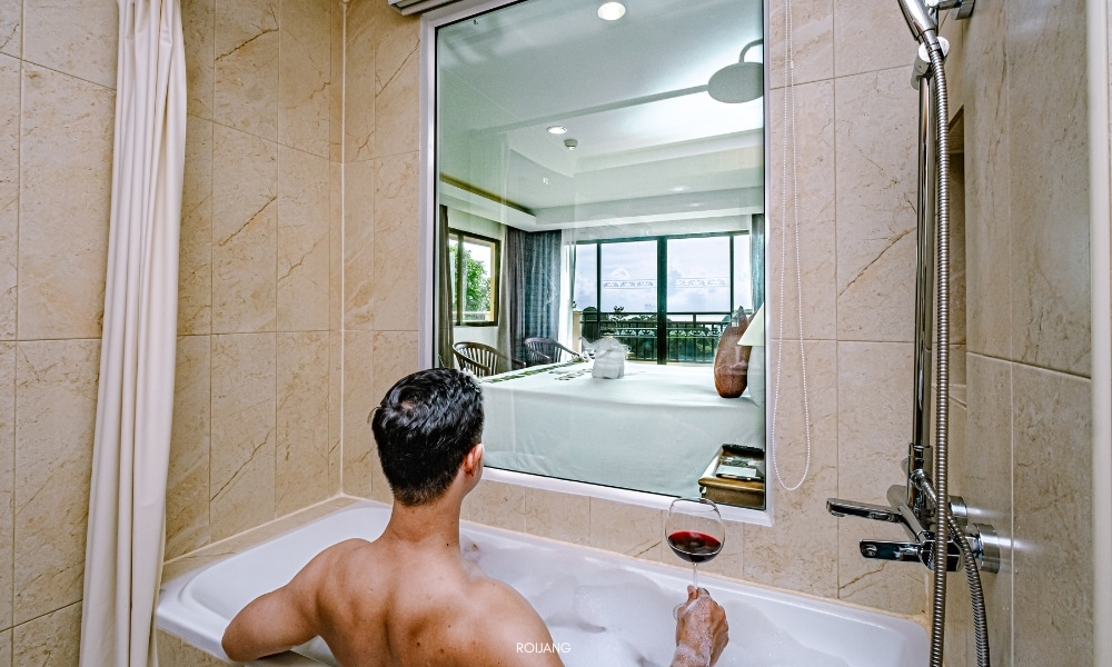 ผู้ชายกำลังนั่งอยู่ในอ่างอาบน้ำที่ชนาลัย การ์เดน รีสอร์ท โดยมีกระจกอยู่ข้างหน้า Chanalai garden resort