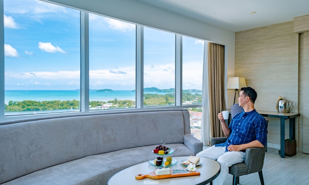 ผู้ชายกำลังนั่งอยู่ในห้องพักของโรงแรมที่โรงแรมโนโวเทล ภูเก็ต ซิตี้ โภคีธรา พร้อมวิวทะเล Novotel phokeethra Phuket