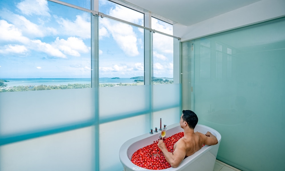 ผู้ชายกำลังนั่งอยู่ในอ่างอาบน้ำของโนโวเทล โภคีธรา ภูเก็ต มองออกไปเห็นทะเล Novotel phokeethra Phuket