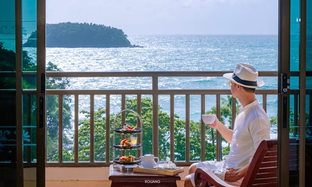 ผู้ชายกำลังนั่งอยู่บนระเบียงที่ชนาลัย การ์เดน รีสอร์ท มองเห็นทะเล Chanalai garden resort