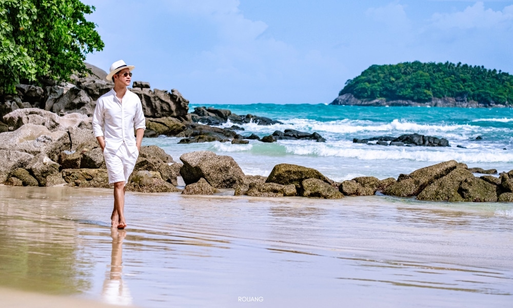 ชายชุดขาวเดินบนชายหาดใกล้โขดหินใกล้ชนาลัย การ์เดน รีสอร์ท Chanalai garden resort
