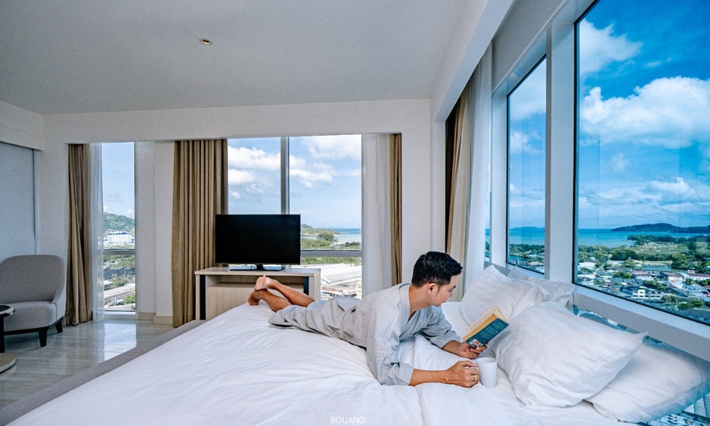 ชายคนหนึ่งนอนอยู่บนเตียงพร้อมชมวิวทะเลที่โรงแรมโนโวเทล ภูเก็ต ซิตี้ โภคีธรา Novotel phokeethra Phuket