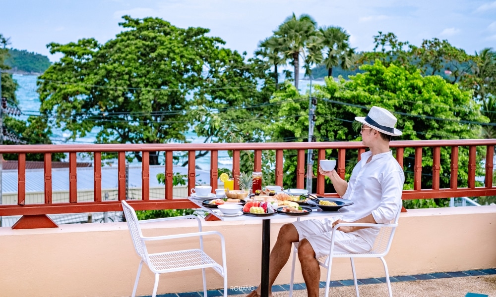 ผู้หญิงกำลังเพลิดเพลินกับอาหารเช้าแสนอร่อยบนระเบียงที่มองเห็นวิวทะเลที่ชนาลัย การ์เดน รีสอร์ท Chanalai garden resort