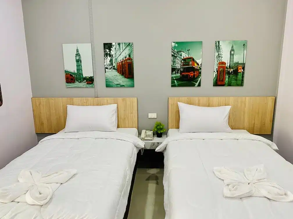 เตียงสองเตียงในหอพักพัทลุงพร้อมภาพวาดสองภาพบนผนัง โรงแรมสุพรรณบุรี