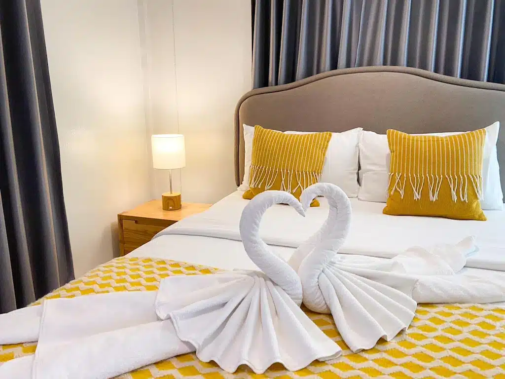 เตียงแสนสบายหรือเตียงในห้องพักพร้อมผ้าเช็ดตัวที่ทำเป็นรูปหงส์ที่โรงแรมแห่งหนึ่งในนครศรีธรรมราช โรงแรมในเมืองนครศรีธรรมราช
