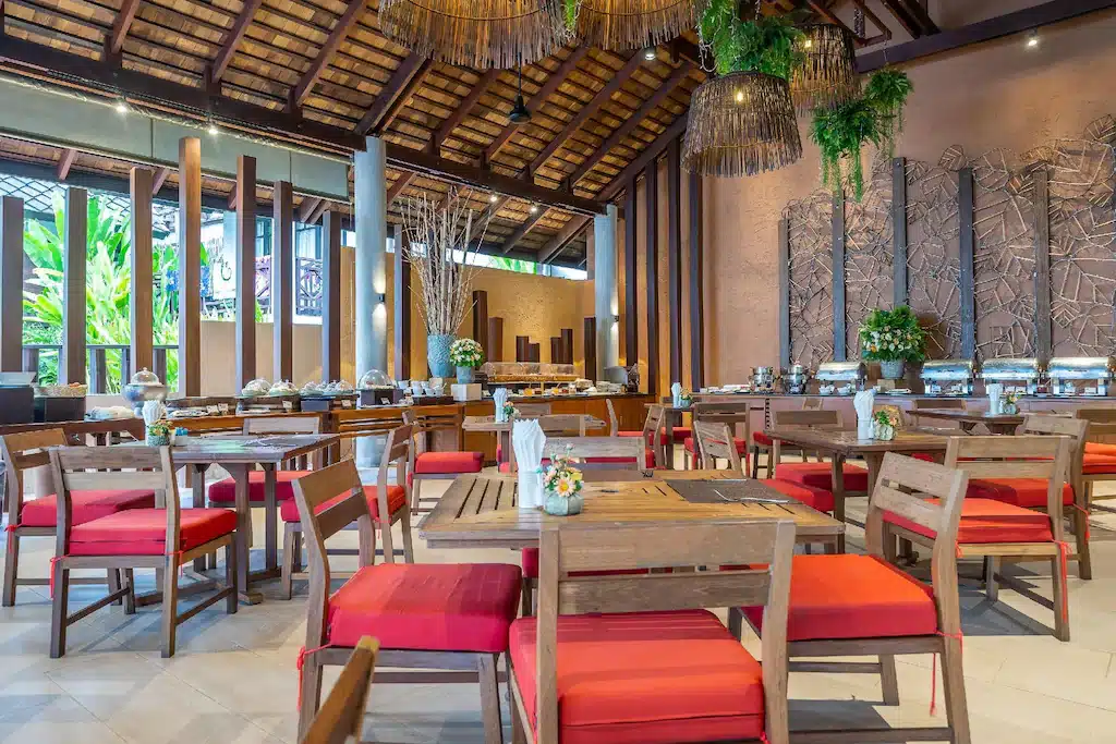 ร้านอาหารที่มีเก้าอี้สีแดงและโต๊ะไม้ ตั้งอยู่ในโรงแรมแกลง พูลวิลล่าระยอง