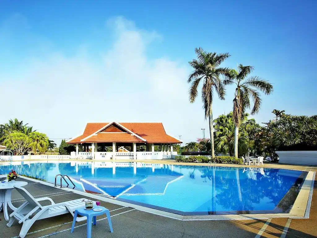 สระว่ายน้ำพร้อมเก้าอี้นั่งเล่นและต้นปาล์มที่โรงแรมแห่งหนึ่งในปทุมธานี ที่พักปทุมธานี
