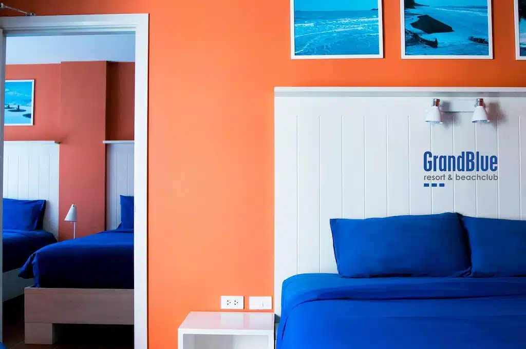 ห้องนอนสีฟ้าและสีส้มพร้อมเตียง 2 เตียงและกระจก เหมาะสำหรับการเข้าพักที่สะดวกสบายหรือการพักผ่อนริมชายหาด ที่พักแกลง