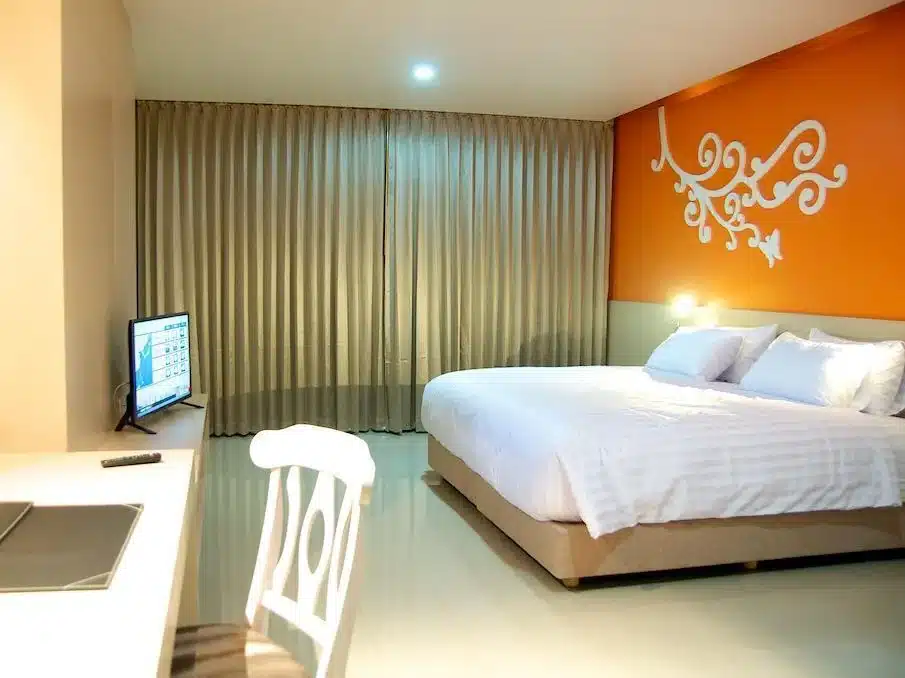 ห้องพัก รีสอร์ทสมุทรสาคร ที่มีผนังสีส้มและเตียงสีขาว ที่เที่ยวสมุทรสาคร