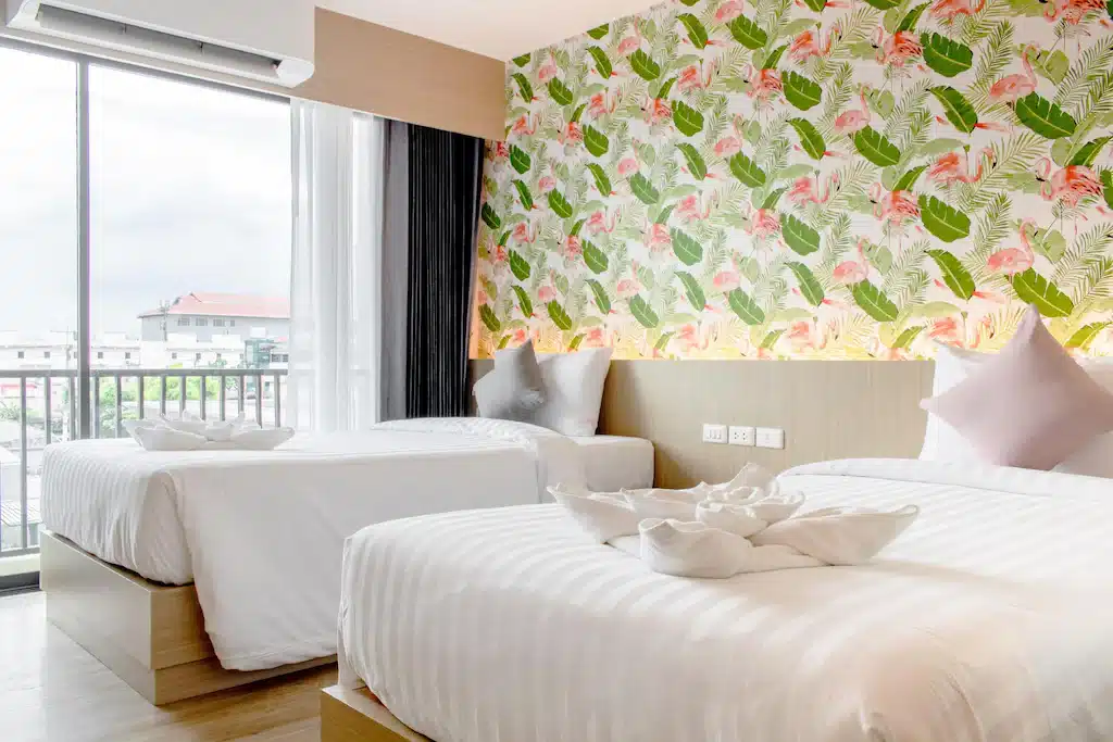 เตียงสองเตียงในห้องพักของโรงแรมที่มีวอลเปเปอร์ลายดอกไม้ตั้งอยู่ในปทุมธานี ที่พักปทุมธานี