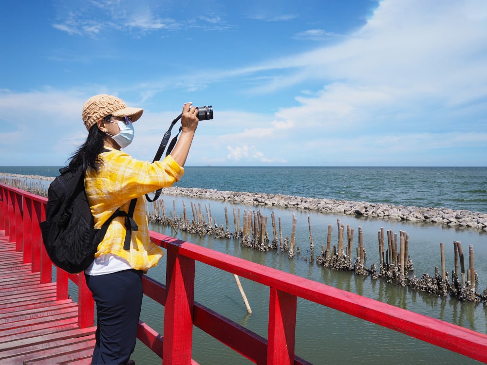 ผู้หญิงสวมหน้ากากอนามัยกำลังเก็บภาพความงามของท้องทะเลขณะเยือนราชบุรีที่เที่ยว