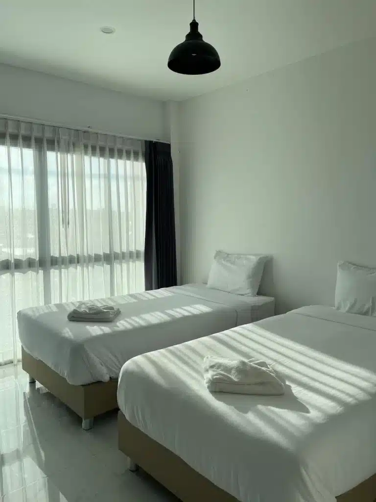 เตียงสองเตียงในรีสอร์ทร้อยเอ็ดพร้อมผ้าปูที่นอนสีขาวและผ้าเช็ดตัว โรงแรมร้อยเอ็ด