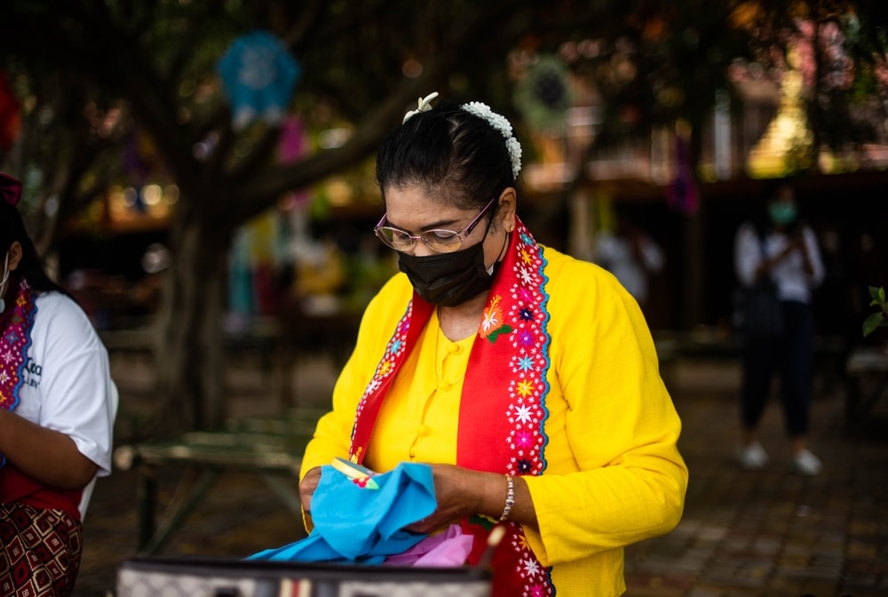 ผู้หญิงสวมหน้ากากอนามัยและถือกระเป๋าขณะสำรวจสวนสวยของราชบุรีที่เที่ยว ที่เที่ยวสวนผึ้ง